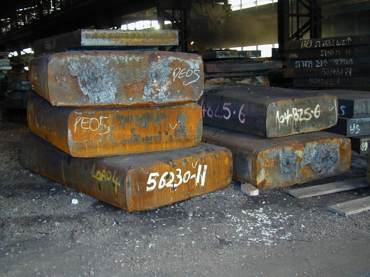 Heavy steel slabs and plate stacked in a yard ready to be cut — representative imagery, not a specific Late Night Fabrication job